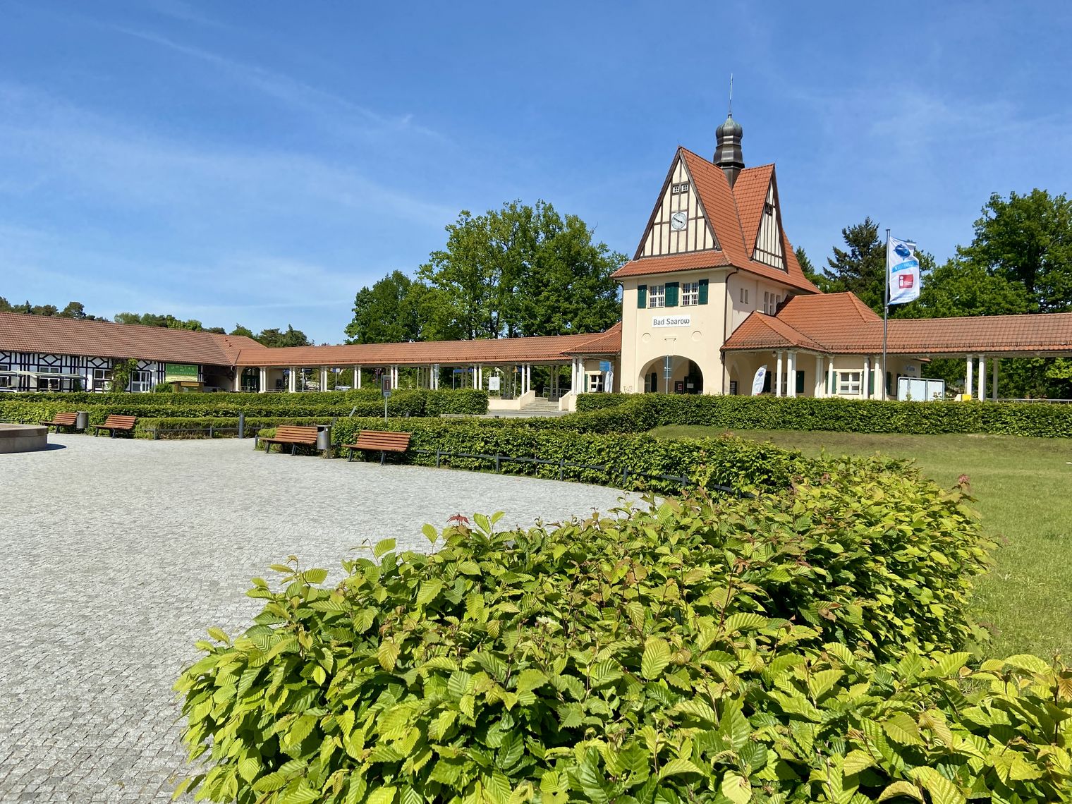 Historisches Bahnhofsbegäude mit Säulenarchitektur aus dem Jahr 1911. Umgeben von einer grünen Hecke. 